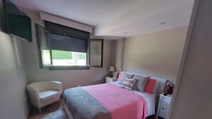 Une chambre à coucher avec un lit, une chaise, une table de chevet, une lampe et une fenêtre.