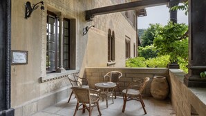 Une terrasse extérieure avec des meubles en osier, un mur en pierre et une vue sur la verdure.