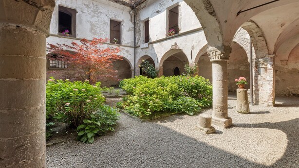 Une cour ancienne, ornée de colonnes de pierre, d’arcades et d’un chemin de gravier.