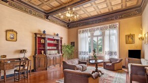 Un salon spacieux avec une cheminée, une grande fenêtre avec des rideaux, une bibliothèque et un lustre.