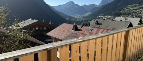 Un balcón de madera con vistas a un pueblo de montaña, con edificios de tejados rojos y un valle cubierto de bosque.