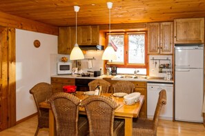 A wooden interior with a dining table, chairs, kitchen appliances, and a window with a view. - Apartment 'Appartement Super Chatel' with Mountain View, Balcony and Wi-Fi (Châtel)