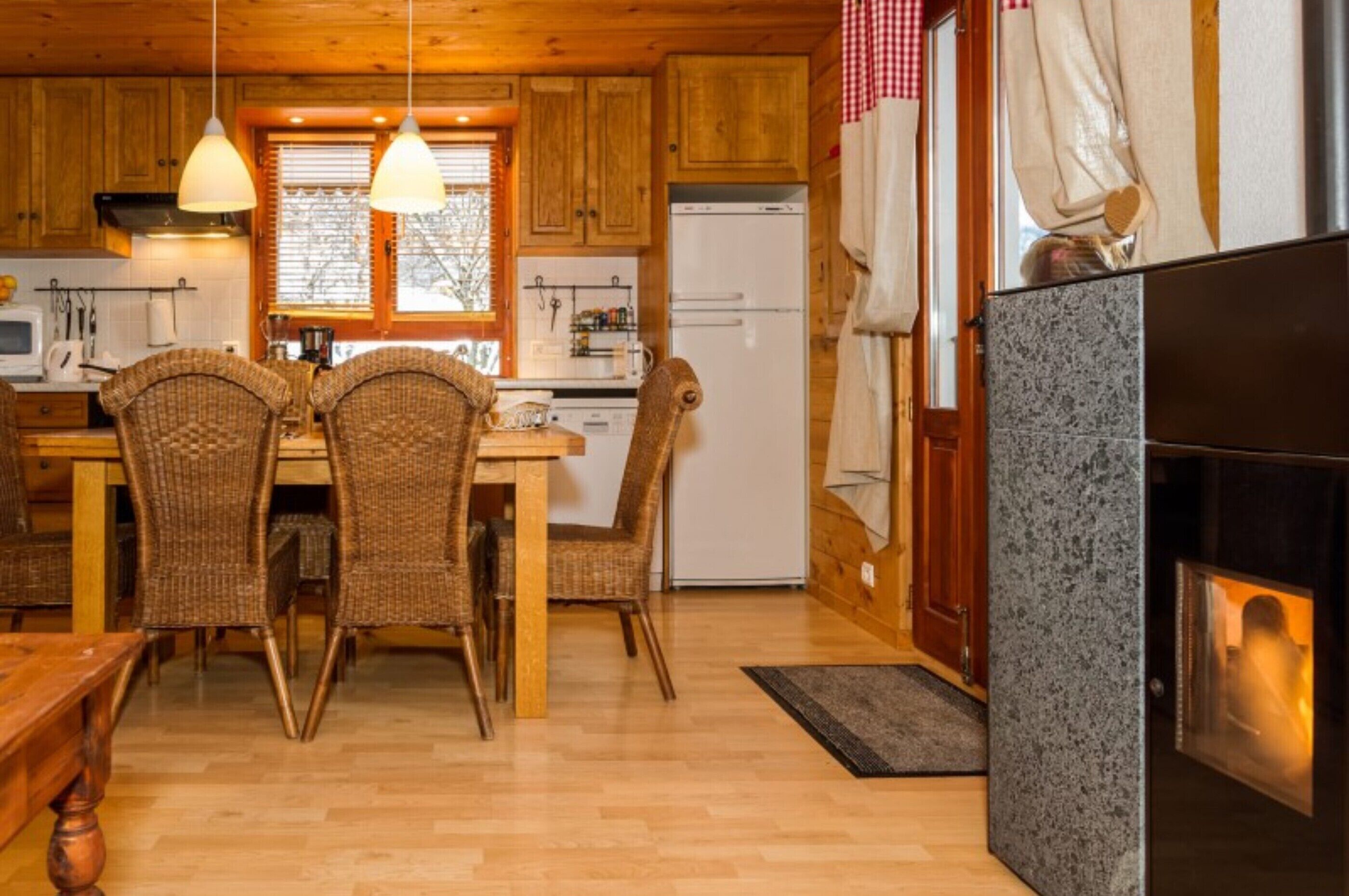 Een houten interieur met een eettafel, stoelen, een koelkast en een open haard.