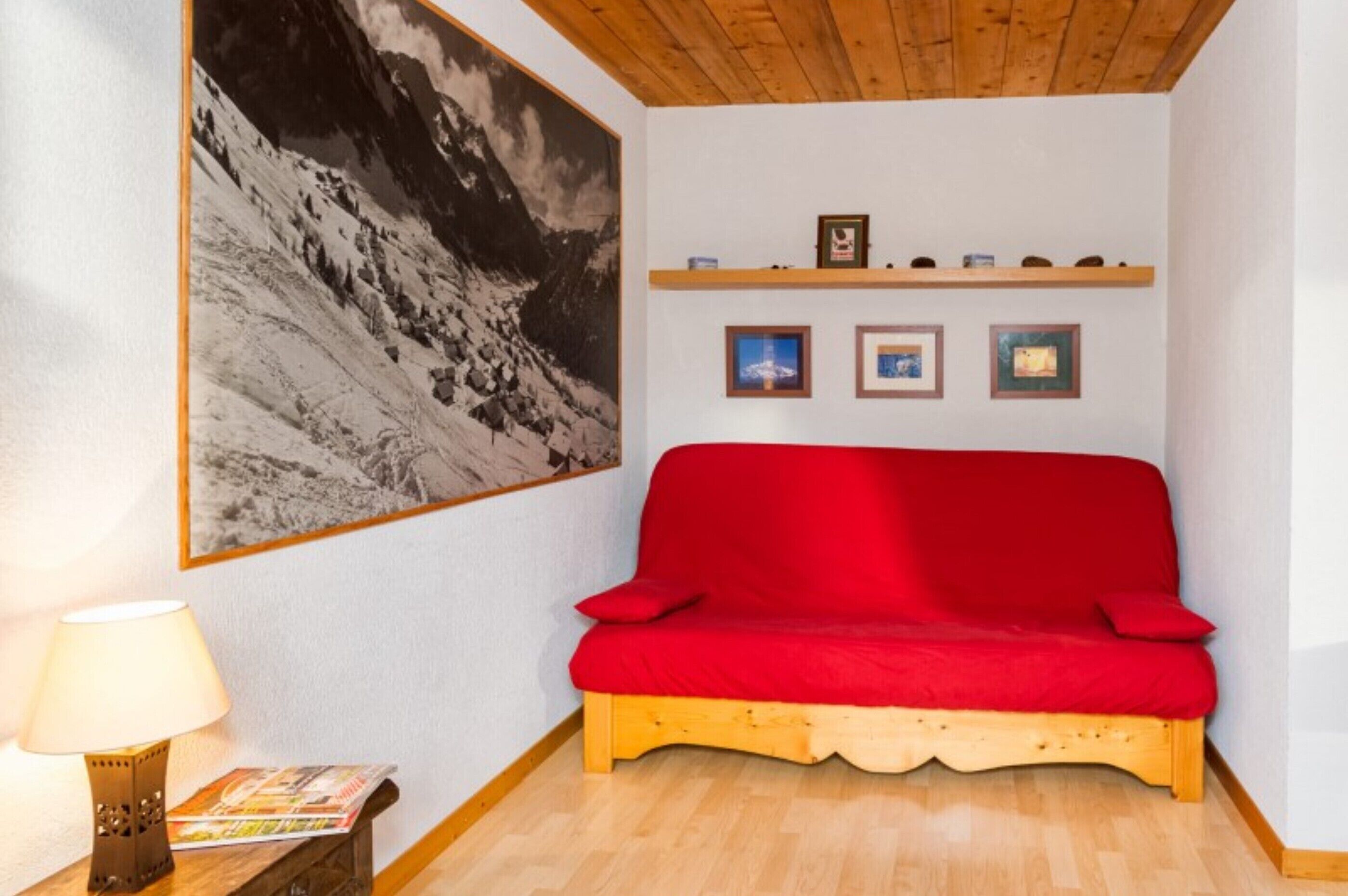 A red sofa, wooden floor, a wall-mounted picture, and a small table with a lamp.