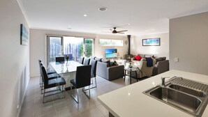 A modern living room with a dining area, a kitchen with a sink, and a large window overlooking a balcony. - Casa Laut; Sleeps 6, Walk to beach, Family Friendly, Pets welcome (Indented Head)