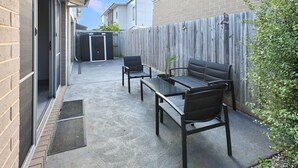 A patio with a table and chairs, a wooden fence, and a building in the background. - Casa Laut; Sleeps 6, Walk to beach, Family Friendly, Pets welcome (Indented Head)