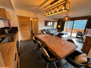 A modern kitchen with a wooden table and chairs, a dining area with a sofa, and a balcony with a view.