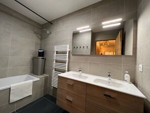 Une salle de bain moderne avec une baignoire, deux lavabos, un miroir et un porte-serviettes.