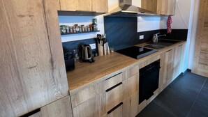 A modern kitchen with wooden cabinets, a black countertop, a built-in oven, and a stainless steel range hood. - Apartment 'Petite Grange 202' with Mountain View, Private Terrace and Wi-Fi (Unknown)