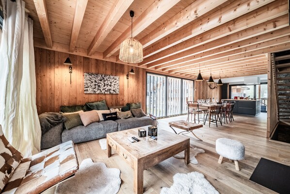A spacious living area with a wooden ceiling, a sofa, a coffee table, and a dining area with chairs and a table.