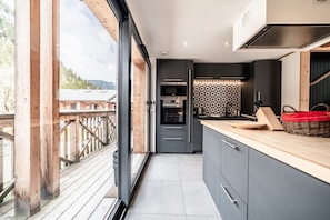 A modern kitchen with a large window, a wooden deck, and a view of the surrounding landscape.