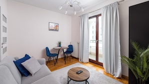 Una sala de estar moderna con un sofá gris, sillas azules, una mesa de centro redonda y una zona de comedor con una mesa pequeña y sillas.