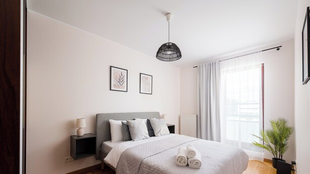 Un dormitorio moderno con una cama grande, mesitas de noche, una lámpara colgante y una ventana con cortinas.