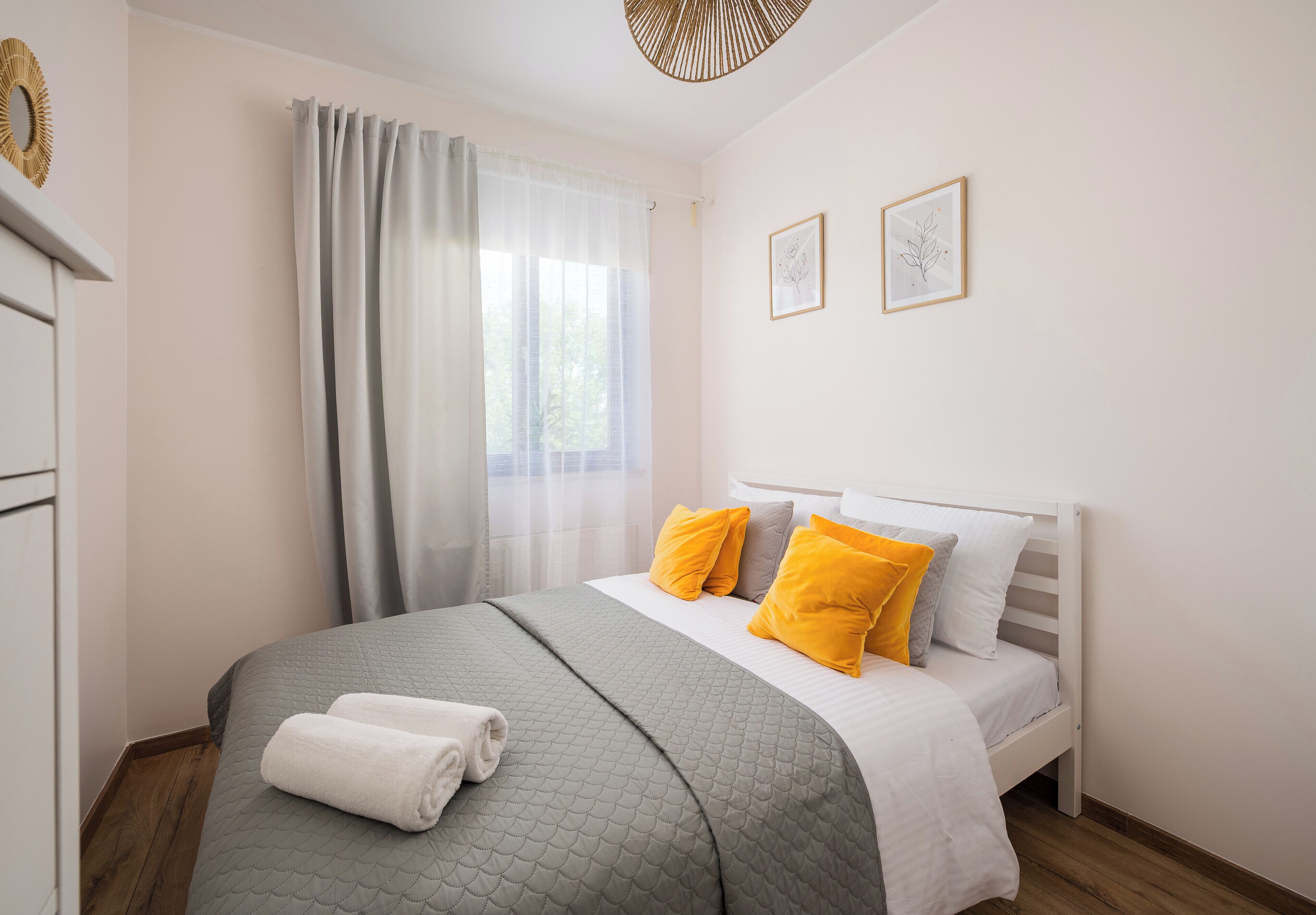 Una cama bien hecha con un edredón gris, dos almohadas amarillas y una toalla blanca al lado.