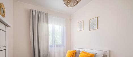 Una cama bien hecha con un edredón gris, dos almohadas amarillas y una toalla blanca al lado.