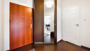 A hallway with a wooden door, a mirrored closet door, and a white door leading to a dining area.