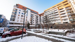 A multi-story residential building with balconies, a covered outdoor seating area, and a snow-covered ground.
