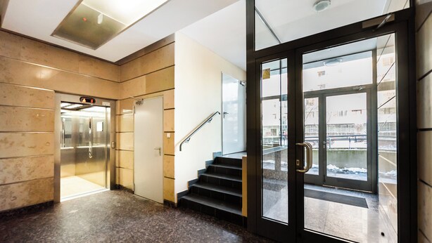 A modern elevator and staircase in a building lobby with a glass door leading outside.