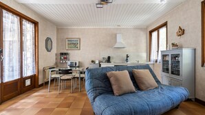 Una habitación con sofá azul, una mesa de comedor, sillas, una zona de cocina y un armario.