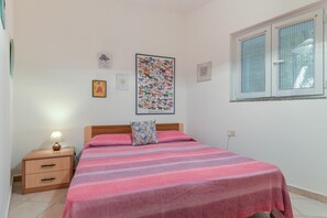 Un dormitorio con cama, mesita de noche, un cuadro en la pared y ventana con vistas.