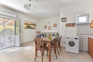 Un comedor con mesa y sillas, una lavadora y un ventanal corredera que da a un espacio exterior.