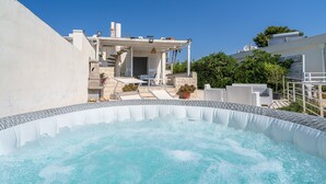A hot tub with a clear view of a building with a pergola and outdoor seating.