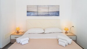 A neatly made bed with two pillows, two bedside lamps, and a painting of a seascape above the headboard.
