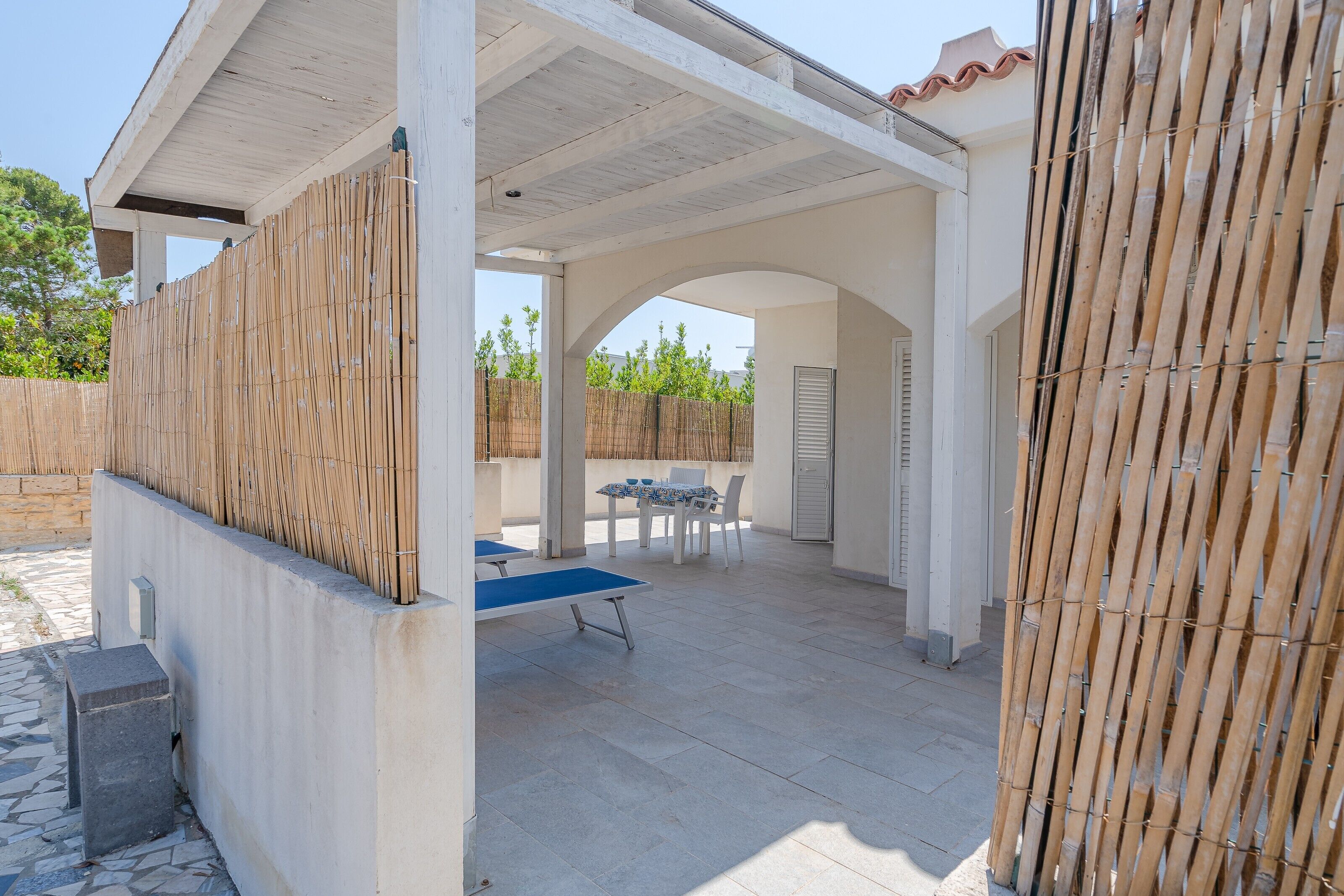 An outdoor patio with a table and chairs, a covered area with a bamboo fence, and a stone-tiled floor.