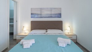 Habitación de hotel con cama, dos lámparas de noche, un cuadro sobre la cama y vista al mar a través de la ventana.