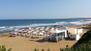 Un hotel frente a la playa con mesas al aire libre, una torre de salvavidas y vistas al océano.