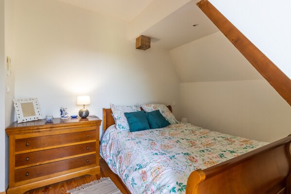 A bedroom with a wooden dresser, a bed with floral bedding, a nightstand with a lamp, and a small decorative item on the dresser.