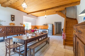 A wooden dining table with benches, a kitchen area with a refrigerator, and a staircase.