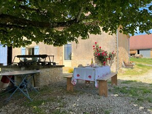 An outdoor dining area with a table set for two, a gas stove, and a flower arrangement.