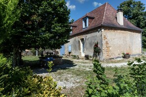 A stone house with a tiled roof, a garden with a bench, and a clear sky.