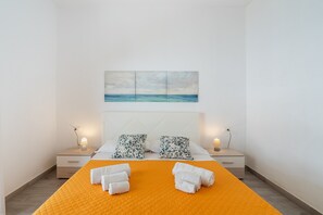 Una camera d'albergo con un letto, due comodini, un quadro raffigurante il mare e asciugamani sul letto.