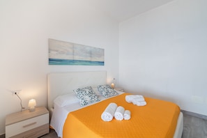 Quarto de hotel com cama, almofadas, mesa de cabeceira, abajur e um quadro na parede.