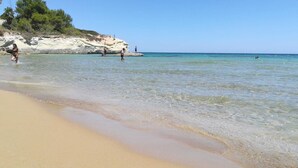 Une plage à l’eau claire, avec un rivage sablonneux et des falaises rocheuses.