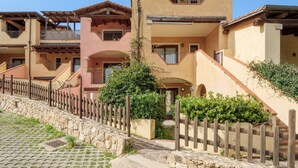 A multi-story building with balconies, a stone wall, and a wooden fence. - Holiday Home 'Orizzonti 33' with Sea View, Private Terrace and Air Conditioning (Golfo Aranci)