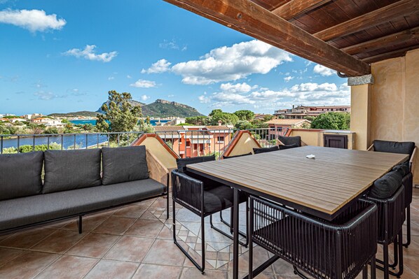 Una terraza con una mesa y sillas de madera, un sofá y vistas a edificios y una colina.