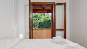 Une chambre à coucher avec un lit, une table de chevet, une fenêtre donnant sur un paysage verdoyant et une porte.