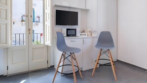 A small kitchenette with a TV, microwave, and cabinets, two grey chairs, and a door leading to an outdoor balcony. - Apartment 'Liolà' with Mountain View, Wi-Fi and Air Conditioning (Scicli)