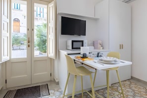 A modern kitchen with a flat-screen TV, microwave, and a dining area with yellow chairs.