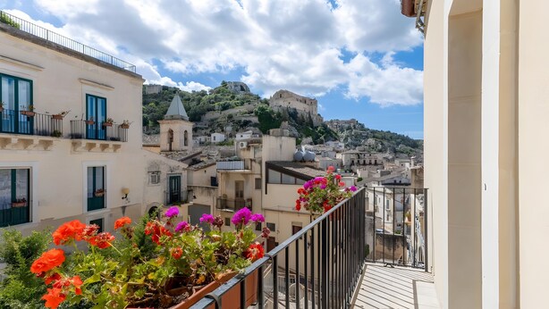 A balcony with potted flowers, a view of a historic building on a hill, and a clear sky. - Apartment 'Liolà' with Mountain View, Wi-Fi and Air Conditioning (Scicli)