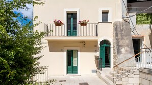A two-story building with a balcony, green doors, and potted plants. - Apartment 'Liolà' with Mountain View, Wi-Fi and Air Conditioning (Scicli)
