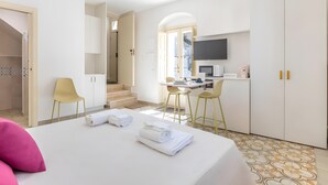 A hotel room with a bed, a desk, two chairs, a TV, and a kitchen area. - Apartment 'Liolà' with Mountain View, Wi-Fi and Air Conditioning (Scicli)