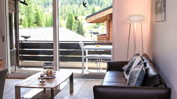 Una sala de estar moderna con una mesa de madera, un sofá de cuero y vistas a un paisaje montañoso a través de grandes puertas de vidrio.