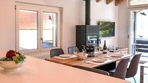 Un comedor con una mesa larga, sillas, un bol de fruta, una estufa y un televisor en la pared.