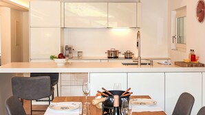 Una cocina moderna con armarios blancos, techo de madera y comedor con una mesa dispuesta para dos personas.