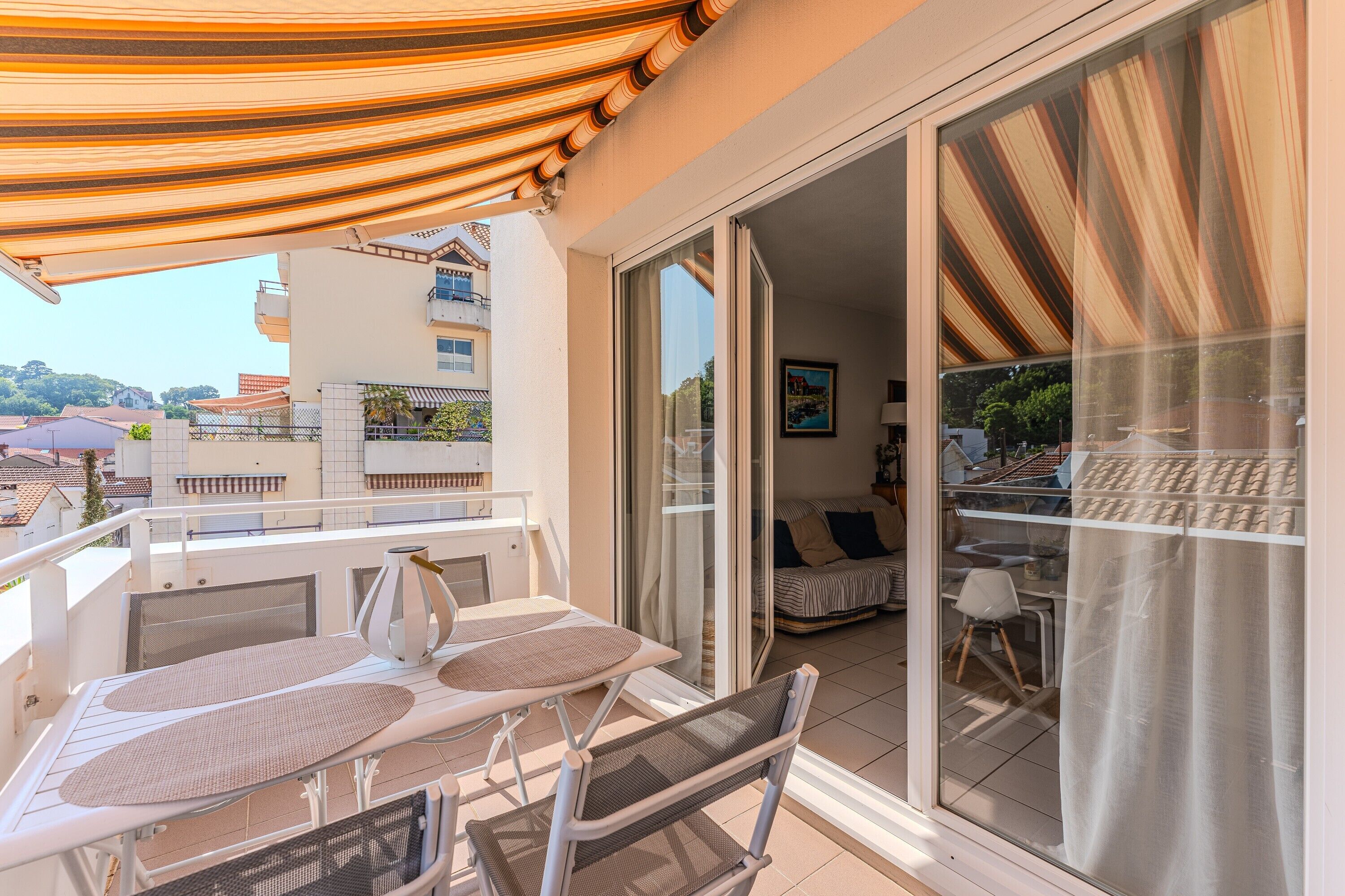 Un balcone con tavolo e sedie, un tendone a righe e vista sull'interno tramite una porta vetrata.