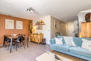 A modern living room with a sofa, dining table, and chairs. There is a staircase leading to another level.